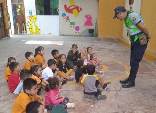 NIÑOS SENTADOS EN EL PATIO DE LA ESCUELA ESCUCHANDO A UN POLICIA ATENTAMENTE